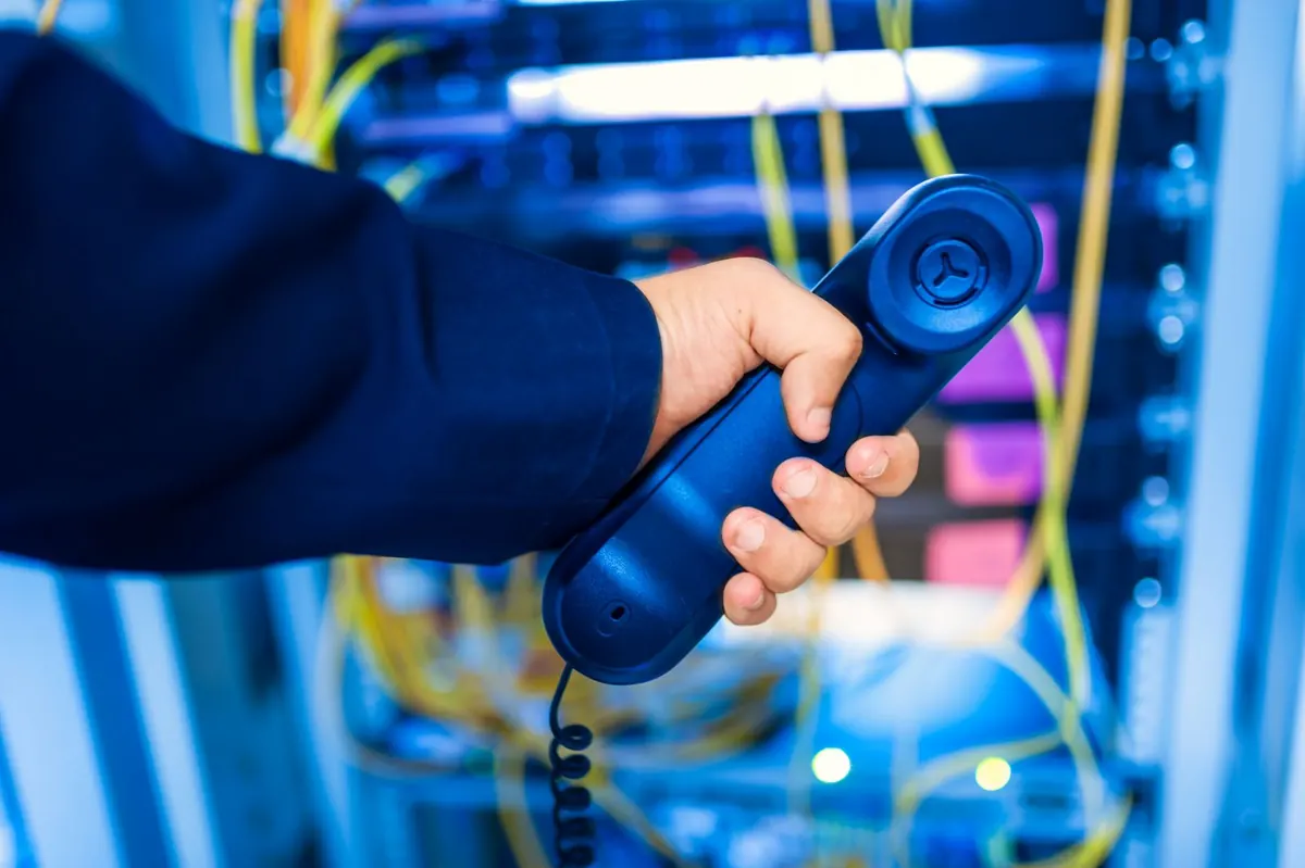 Installazione di centralino VoIP a Latina: mano che impugna la cornetta di un telefono davanti all'armadio di rete